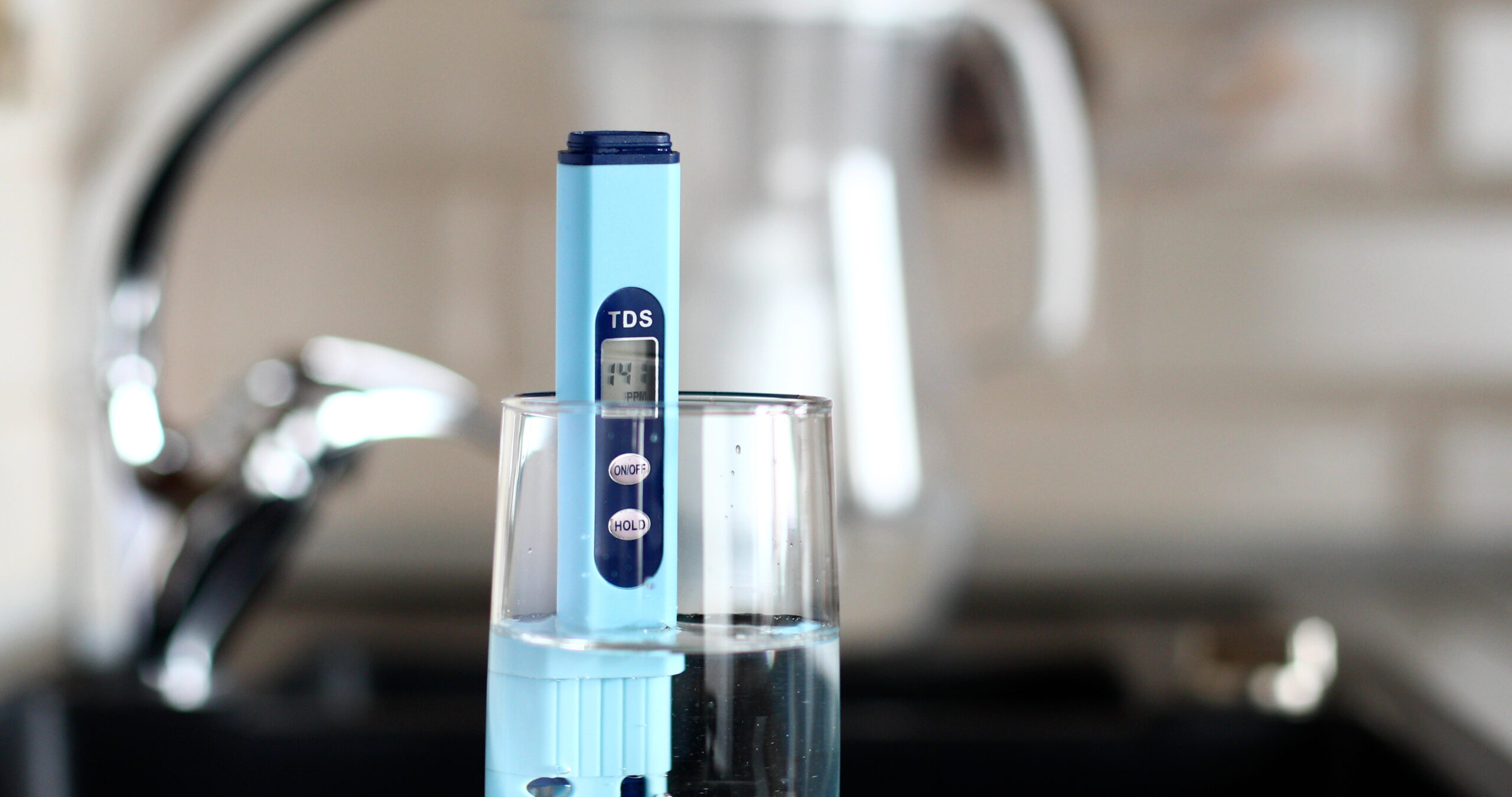 measurement of tds of water. electronic ph meter in a glass of water.filter for water purification. there is a tap for drinking water in the background.